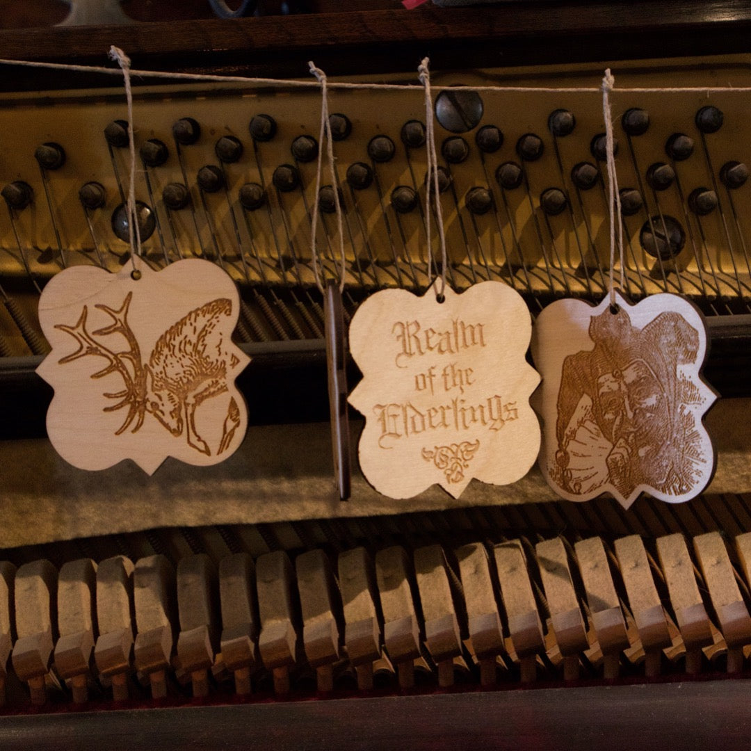 3 - Realm of the Elderlings Baltic Birch Ornaments hung in front of piano soundboard.